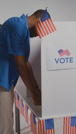 Vertical-Video-Shot-Of-Man-Walking-Into-Booth-With-Ballot-Paper-To-Cast-Vote-In-American-Election---Shot-In-Slow-Motion-1